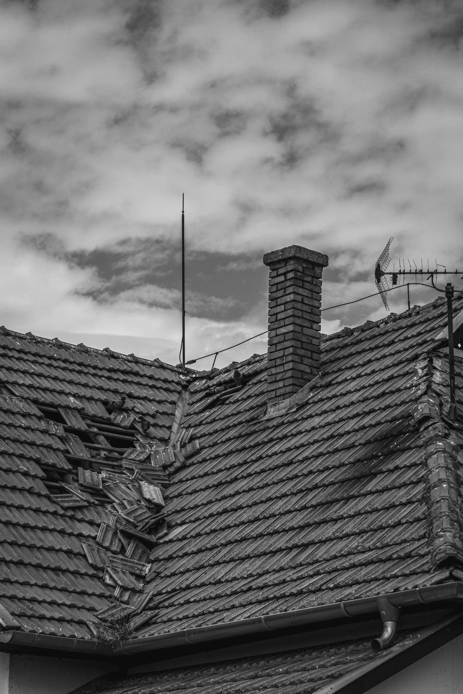 Black and white photo of a tile roof with visible storm damage near the chimney